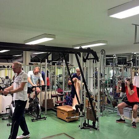 Mehrere Personen trainieren in einem Fitnessraum mit verschiedenen Geräten und Gewichten.