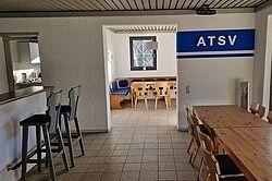 Blick in einen Vereinsraum mit Tischen, Stühlen und einer wandmontierten ATSV-Beschriftung.