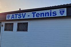 Signage des ATSV Tennis an einer weißen Wand mit Fenstern im Hintergrund und Abendlicht.
