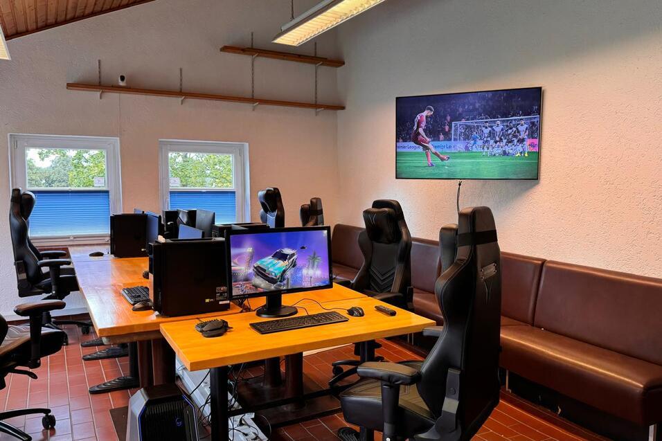 Büro mit mehreren Gaming-PCs und ergonomischen Stühlen, großer Bildschirm zeigt ein Fußballspiel.