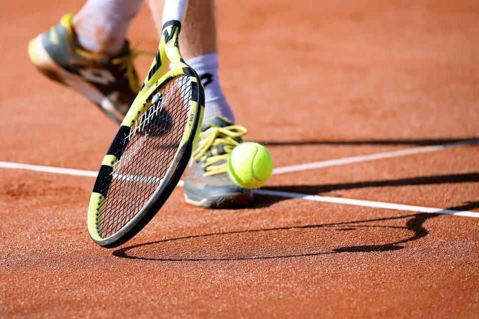 Nahaufnahme eines Tennisballs, der vom Schläger eines Spielers auf einem roten Sandplatz getroffen wird.