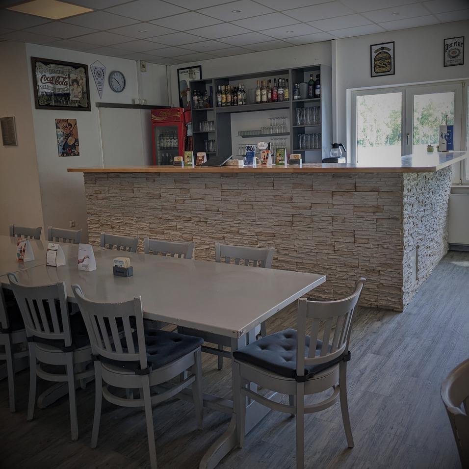 Innenansicht eines Cafés mit einem steinernen Empfangstresen, Stühlen und Theke mit Getränken im Hintergrund.